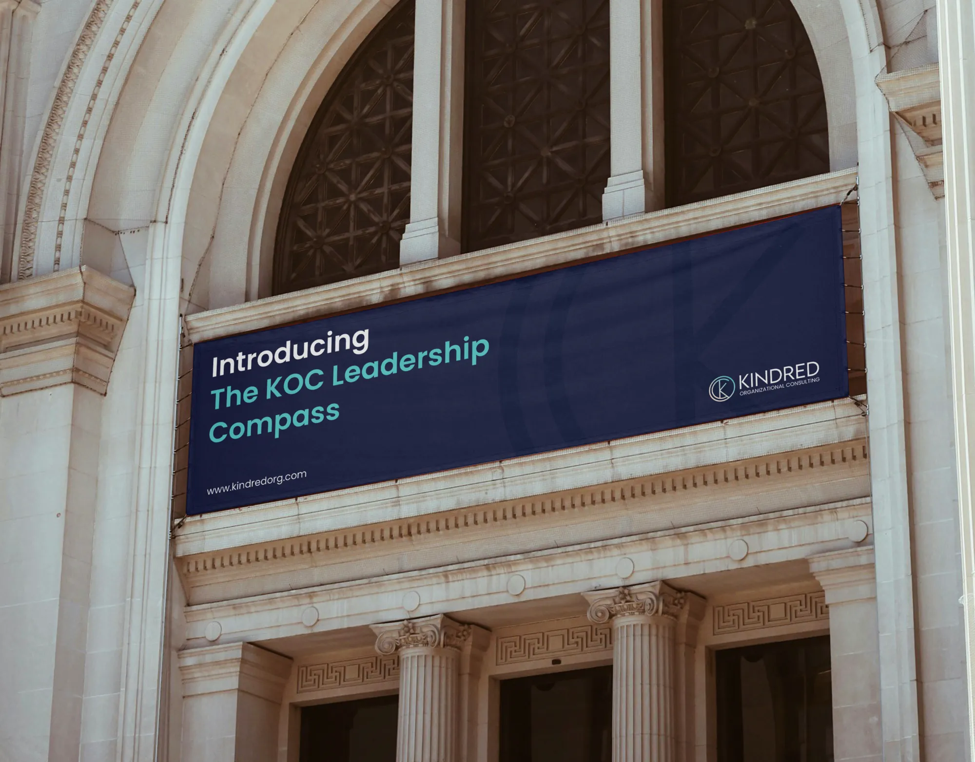 A navy Kindred banner reading Introducing The KOC Leadership Compass, hung across the arched front of a stone building.