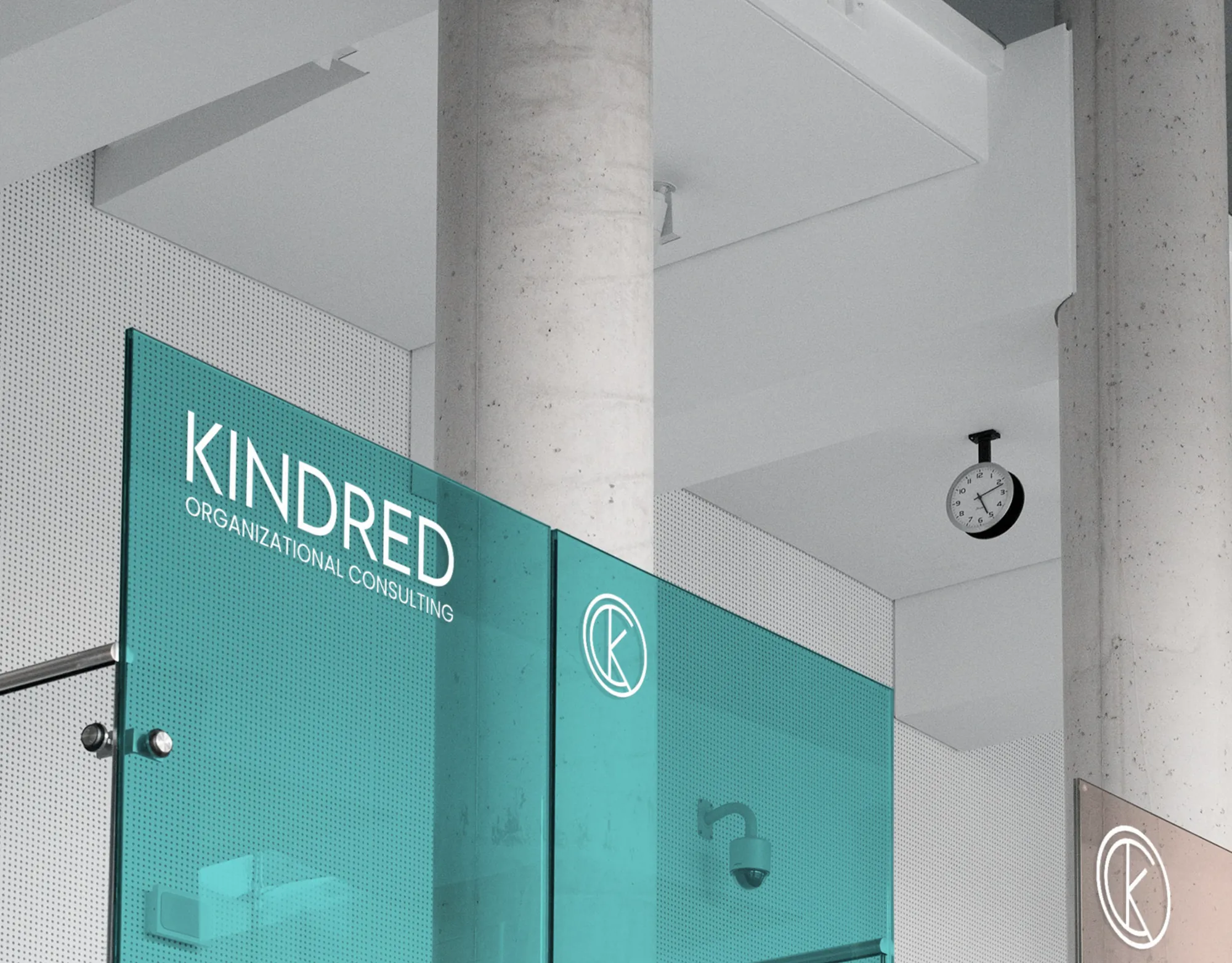 The Kindred wordmark and monogram in white on a teal glass partition in a bright concrete office.